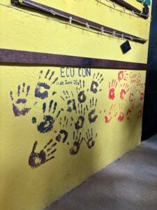 A yellow wall with purple handprints underneath the title "ECU CON 11 de Junio '25".