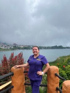 Stephanie standing in purple scrubs with a stethoscope around her neck, standing in front of the river.
