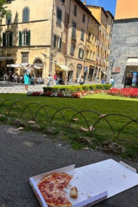 A pizza box lying on the ground, partially open, with remnants of pizza visible inside. 