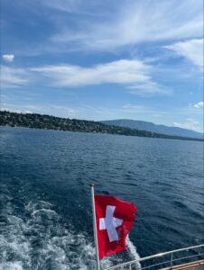 The Swiss flag flying on a boat with the wake in the water behind it.