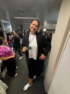Natalia standing in a room with other people holding her name badge and smiling.