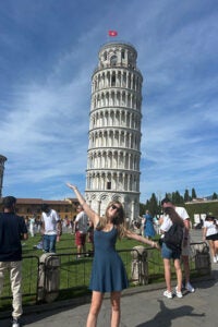 A woman in a dress poses playfully in front of the Leaning Tower of Pisa, showcasing the iconic landmark. 